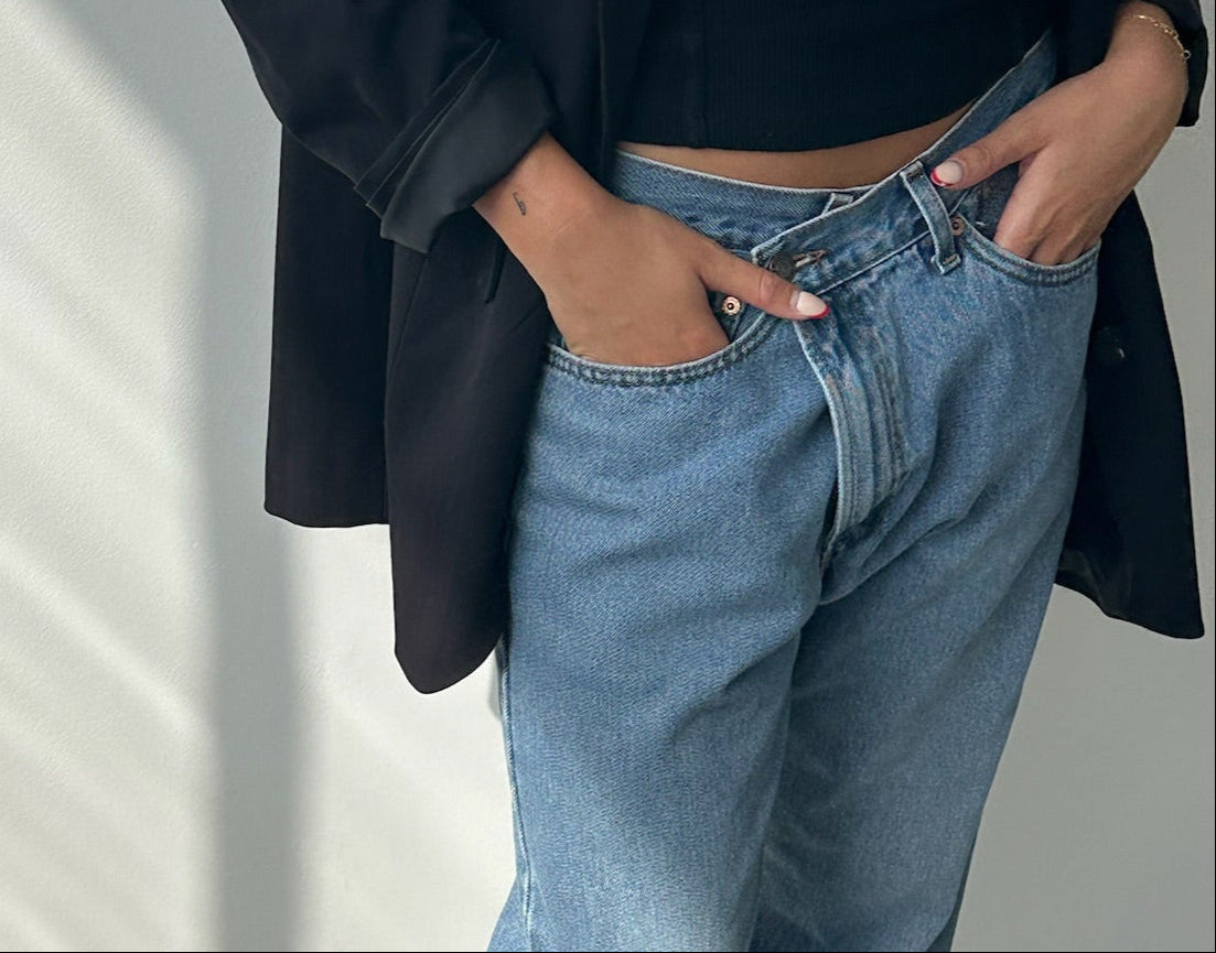 Person wearing blue jeans and a black jacket against a light background